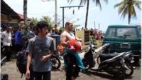 In this handout photograph released by Pikiran Rakyat, an unidentified survivor carrying a child is escorted at a marine police station on the coast of Pangandaran town in Indonesia's West Java province on November 1