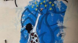 A woman walks past graffiti depicting a young girl trying to reach stars from the EU flag on 18 February 2012 in Athens, Greece