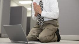 Businessman praying in front of a computer