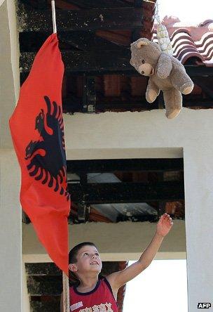 Child reaches up to a teddy bear from a balcony