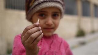A girl shows a sniper's bullet found in her schoolyard in rebel-held Douma, a suburb of Damascus, 12 April 2016
