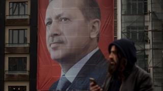 People walk past a large banner showing a portrait of Turkish President Recep Tayyip Erdogan in Taksim Square, Istanbul, 13 March