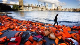 A woman walks past hundreds of refugee life jackets collected from the beaches of Chios, Greece, on the edge of the East River, to call attention to the refugee crisis in Brooklyn, New York, USA, 16 September 2016