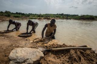 Three men sift through mud with circular sieves