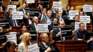 Deputies from the Swiss People's Party hold posters reading "constitutional breach" and "mass immigration continues" after the vote on giving Swiss jobseekers priority in parliament in Bern, Switzerland on 16 December 2016