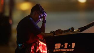 A Dallas police officer, who did not want to be identified, takes a moment as she guards an intersection in the early morning after a shooting in downtown Dallas, Friday, July 8, 2016