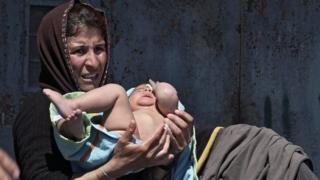 Woman holds her baby in a towel after a bath outside a tent at the port of Piraeus