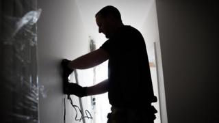 A builder fits a radiator to the wall at a residential development