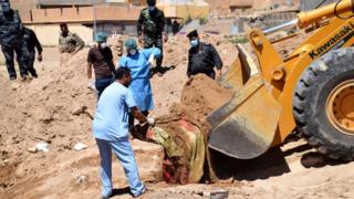 People in forensic suits and masks crowding around a digger