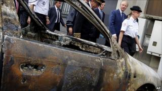 Interior Minister Brice Hortefeux (second from right) passes a charred car in Grenoble, 17 July