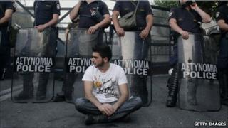 A protester sits in front of riot police during a peaceful ongoing rally against plans for new austerity measures