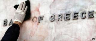A worker cleaning a sign for the Bank of Greece