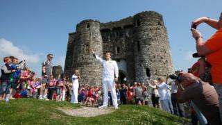 Torchbearer Peter Hale holds the Olympic torch high outside Kidwelly Castle