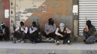Free Syrian Army members, with covered faces and holding weapons, sit by the side of a street in Qaboun district, Damascus June 11, 2012.
