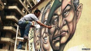 Man in Cairo paints mural depicting toppled President Hosni Mubarak (r) and current military ruler Mohammed Hussein Tantawi as two halves of one face (22 May)