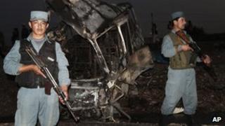 Afghan policemen stand guard near a damaged bus at the scene of the suicide attack in Kandahar