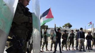Palestinian youth waves a flag in front of Israeli soldiers (29 November 2012)