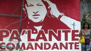Woman walks past a mural depicting Hugo Chavez with the words "Onward, commander"