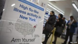 People line up behind a sign advising people against the flu outbreak at a pharmacy in New York 10 January 2013