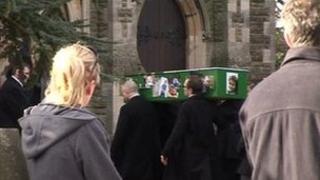 Coffin being carried into church while people stand in the background