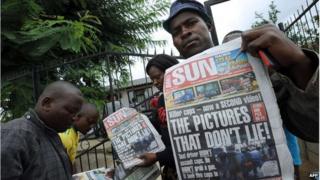 People hold up a newspaper outside the home of Mido Macia, Daveyton, South Africa