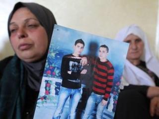 The mother of Moataz Sharawna holds up a picture of him (right, in red and black jumber) (2 July 2013)