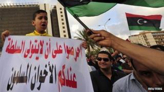 A boy holds a sign that reads: "Do not take power with you, Brotherhood" as protesters wave the Libyan flag during a demonstration against the Muslim Brotherhood for interfering in local politics, in Benghazi, Libya, 10 May 2013