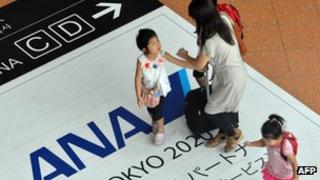 Passengers walking over an ANA logo in Tokyo airport