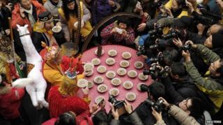 People take pictures of three men (left, from top to bottom) dressed as Zhu Bajie, Tang Dynasty Buddhist monk Xuanzang and Monkey King Sun Wukong, who are all characters from the Chinese classic novel Journey to the West, as they eat laba porridge during the Laba Festival at the Xuanzang Temple in Nanjing, Jiangsu province, 8 January 2014