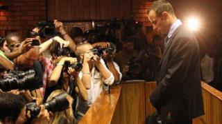 Photographers take photos of Olympic athlete Oscar Pistorius as he stands in the dock during his bail hearing at the magistrates court in Pretoria, South Africa, Friday, 22 February 2013