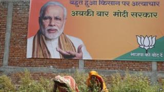 Farmworkers in a field in front of a Modi billboard near Allahabad, the northern Indian state of Uttar Pradesh, India, Sunday, April 6, 2014
