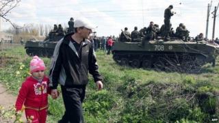 A father and his daughter walk past a column of Ukrainian armoured vehicles in Kramatorsk - 16 April 2014