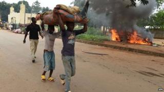 Children carry furniture as they walk past a burning car, set on fire by its owner before leaving the PK12 district, outside of Bangui, on April 27, 2014