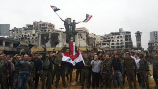 Government forces hang the national flag on top of a pole in the old city of Homs, Syria