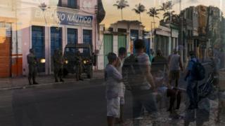 Security and passersby reflected in the glass of a shop window in Salvador, Brazil