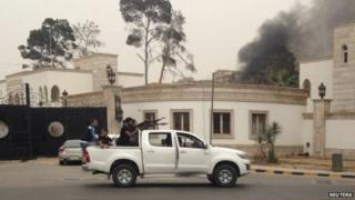 Armed men aim their weapons from a vehicle as smoke rises in the background near the General National Congress in Tripoli 18 May