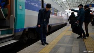 A man looking quizzically down at the yellow line on the train platform