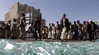 Houthi supporters walk past broken glass at a demonstration in Yemen's capital, Sanaa (22 April 2015)