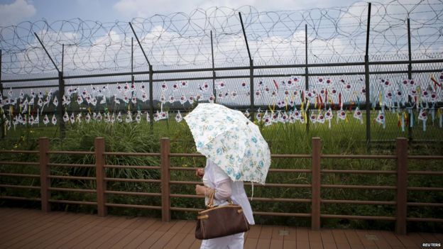 A tourist holding a parasol walks by a barbed-wire fence decorated by South Korean national flags at the Imjingak pavilion near the demilitarized zone separating the two Koreas in Paju, South Korea (22 August 2015)