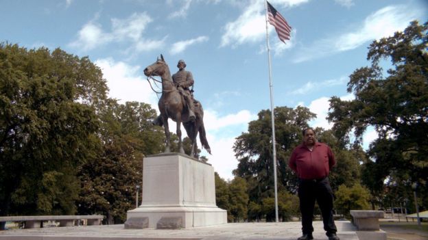 Daryl Davis em frente a um monumento e uma bandeira dos EUA