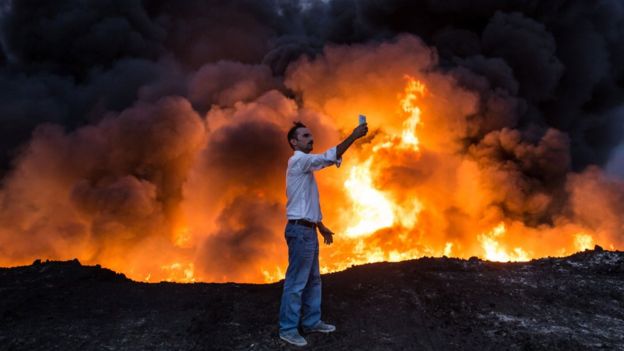 A man takes a selfie in front of flames south of Mosul