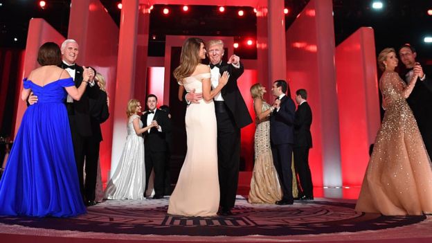 Donald Trump and Melania Trump dance next to other couples at the Inaugural Ball. Mr Trump, in a tuxedo, points towards the crowd.