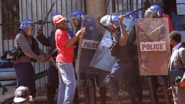 Police with batons clash with protester in red t shirt