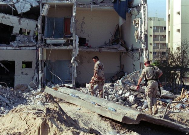 Saudi and US military personnel walk through the remains of the Khobar Towers housing complex after a bomb attack on 27 June 1996