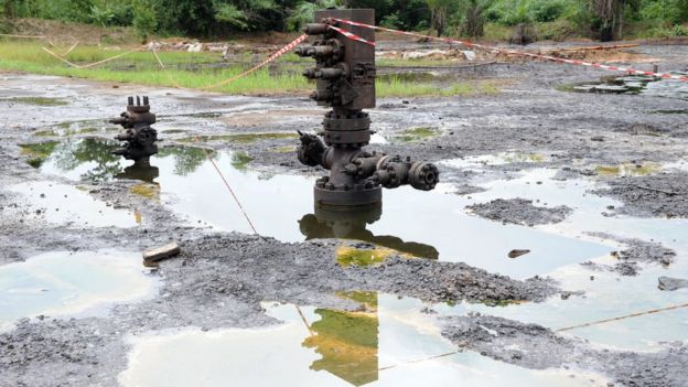 Terra poluída por derramamento de petróleo, com piscinas de óleo.