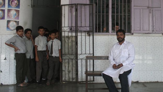 Mr Shaikh sits outside his classroom as his students peep from the door