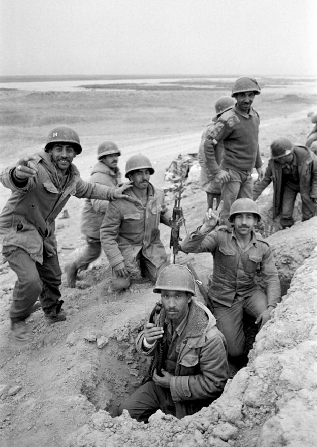 An Iraqi soldier flashes a V-sign as his comrades look on, in a trench dug near Al Boweizah swamps, north of Basra on March 18, 1985