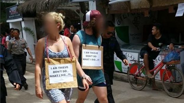 The two foreigners, walking down a small street with signs around their necks.