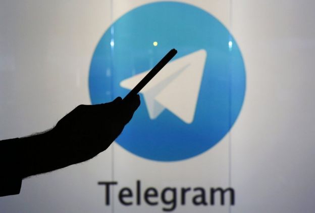 Un hombre sostiene el celular ante el logo de Telegram.