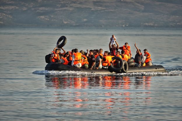 In a dinghy full of Syrian refugees, a man holds a baby aloft